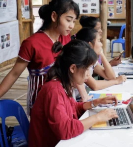 Two Burmese women with one standing and the other seated down in front of a laptop